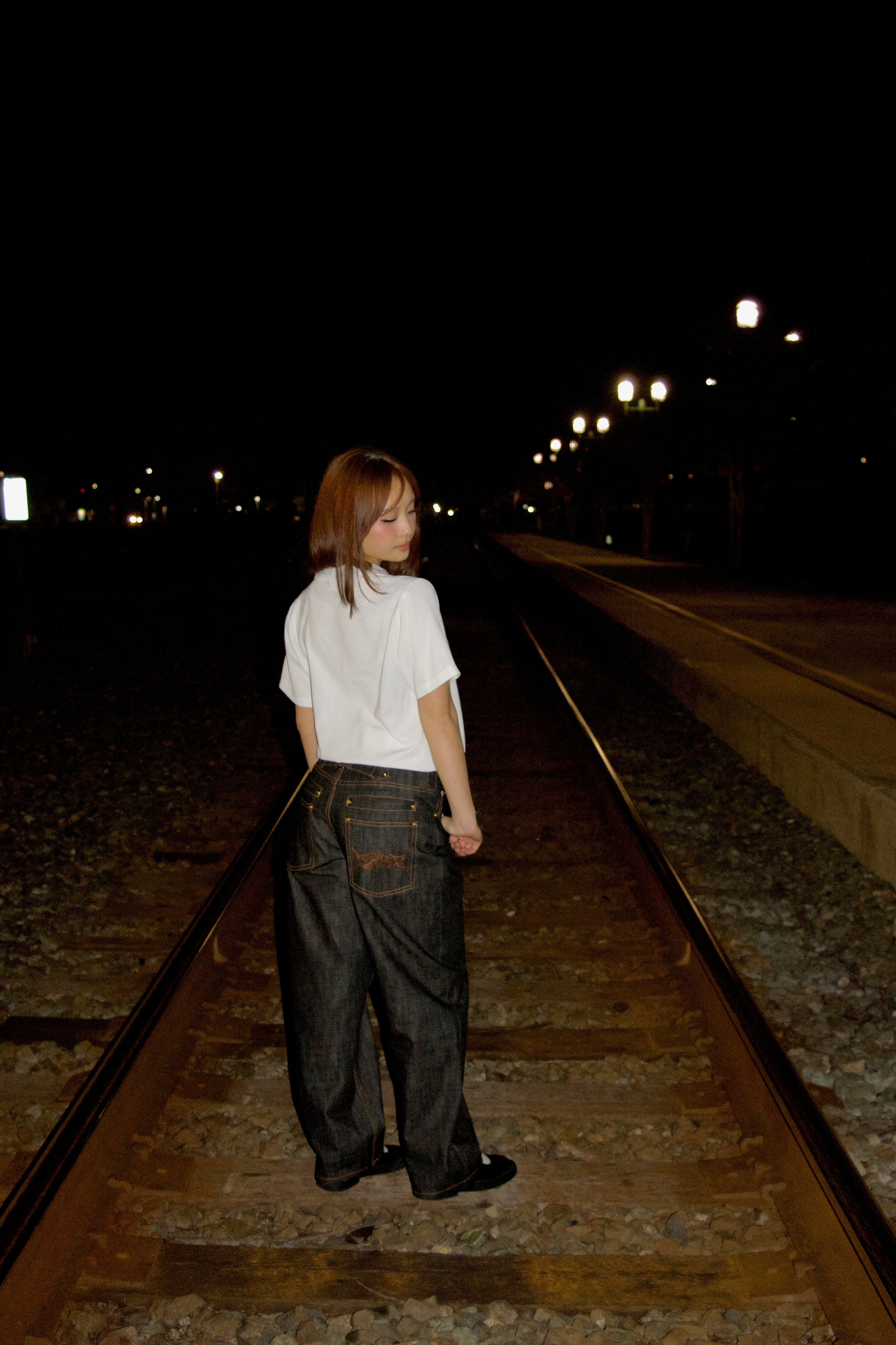 Person standing on train tracks at night with streetlights in the background